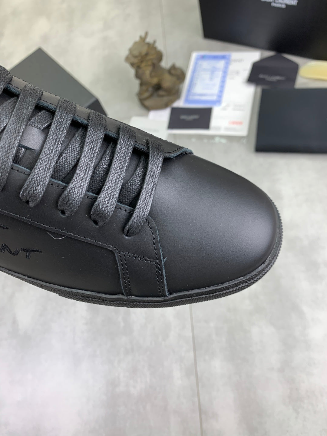 Close-up of dark gray leather sneaker toe with lace-up eyelets and stitching.