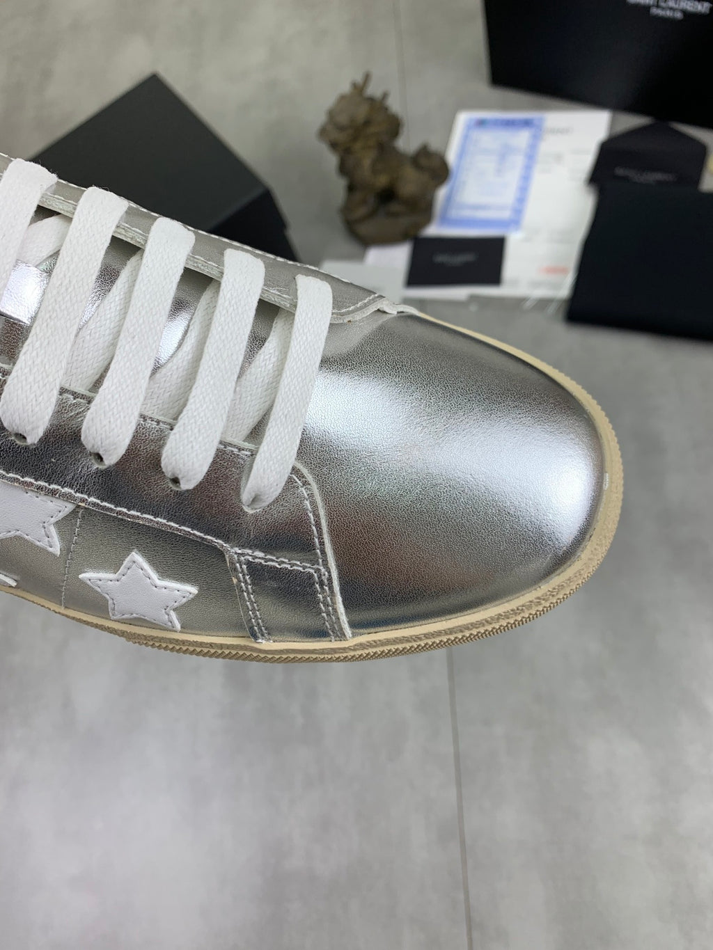 YSL unisex low-top sneaker close-up, silver upper with white star paneling, white laces, gum sole