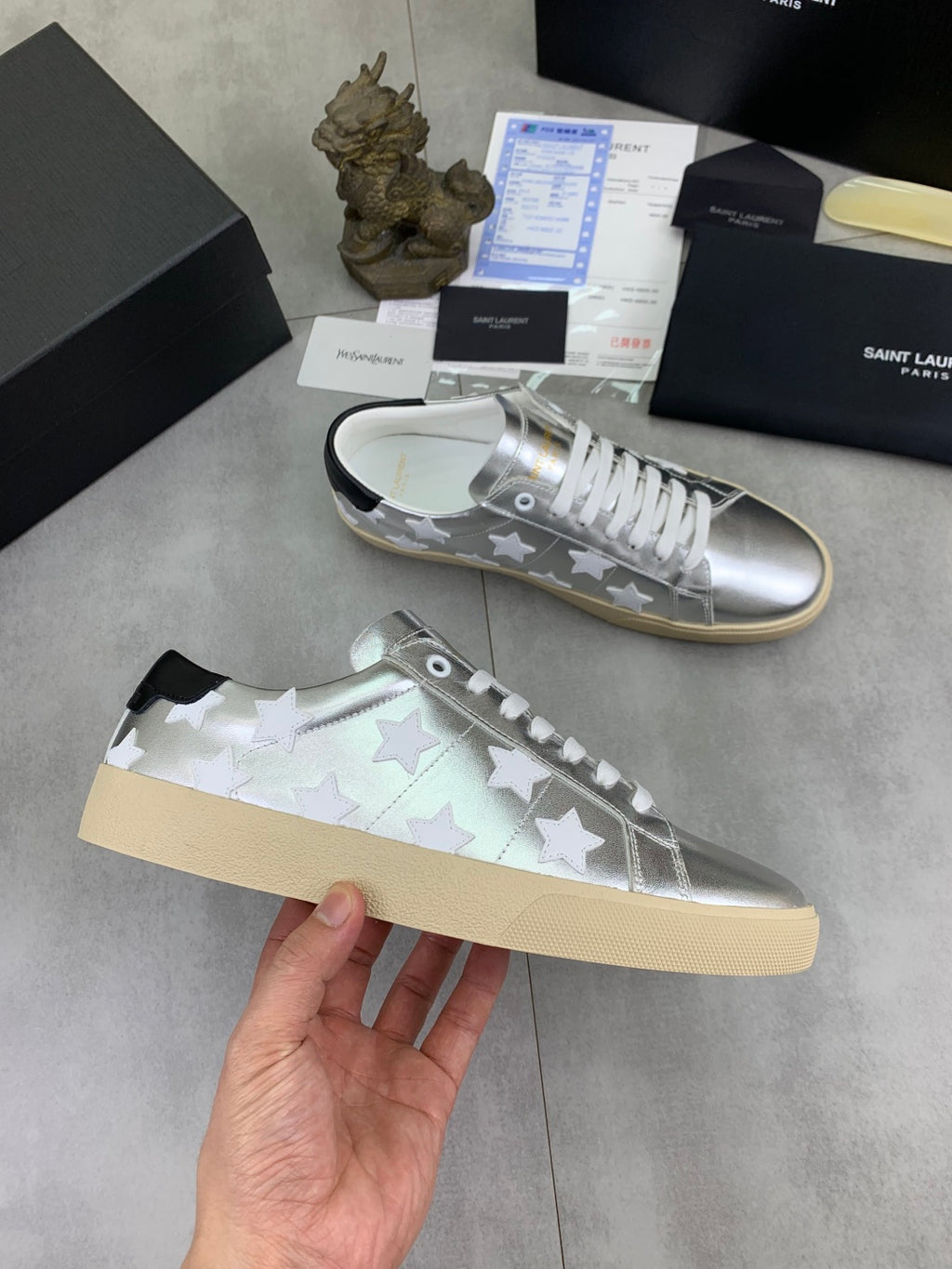 YSL unisex low-top sneakers held in hand, silver with white stars, white laces, gum sole