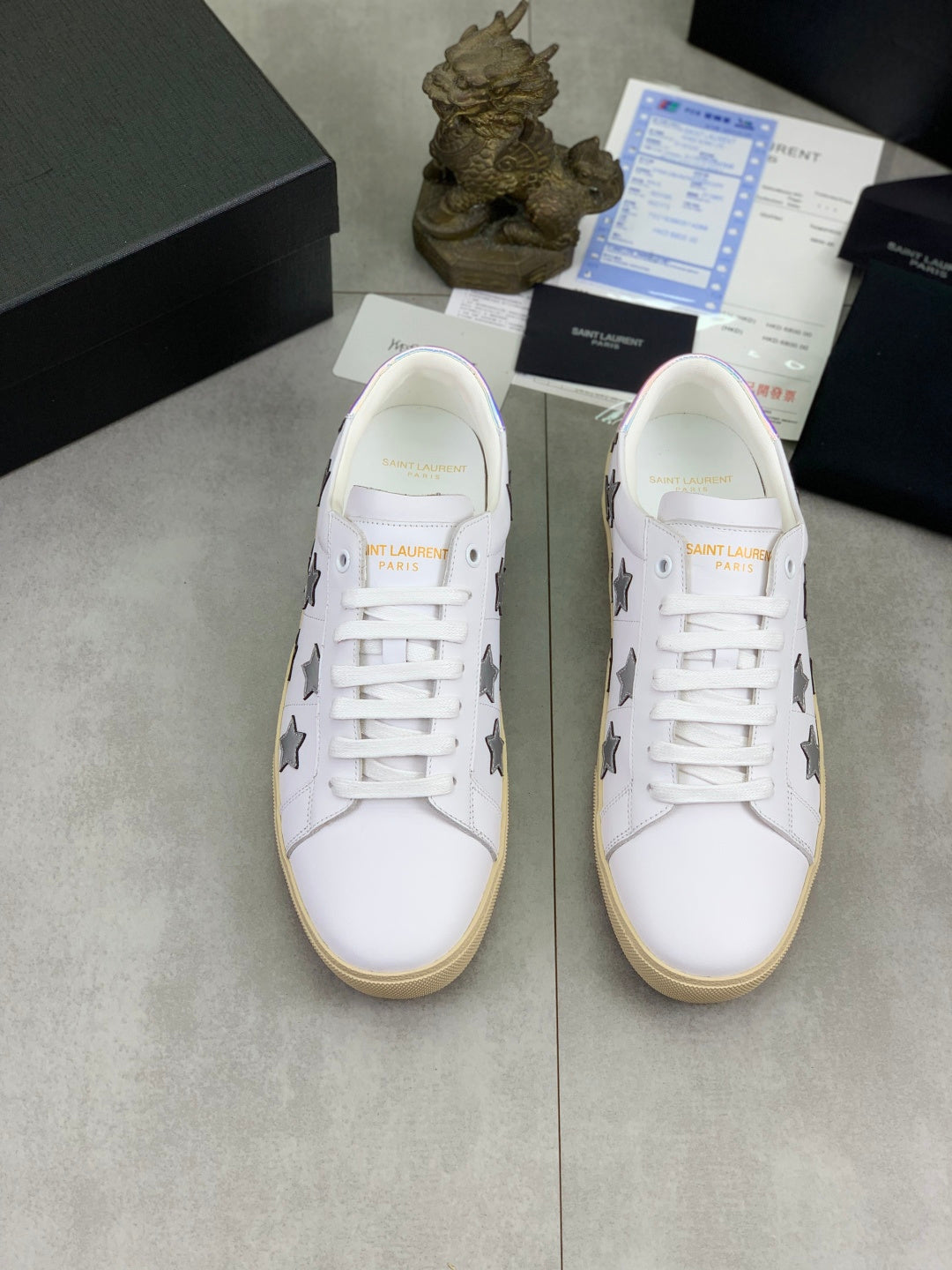 Pair of unisex white sneakers with gray stars and white laces on beige soles