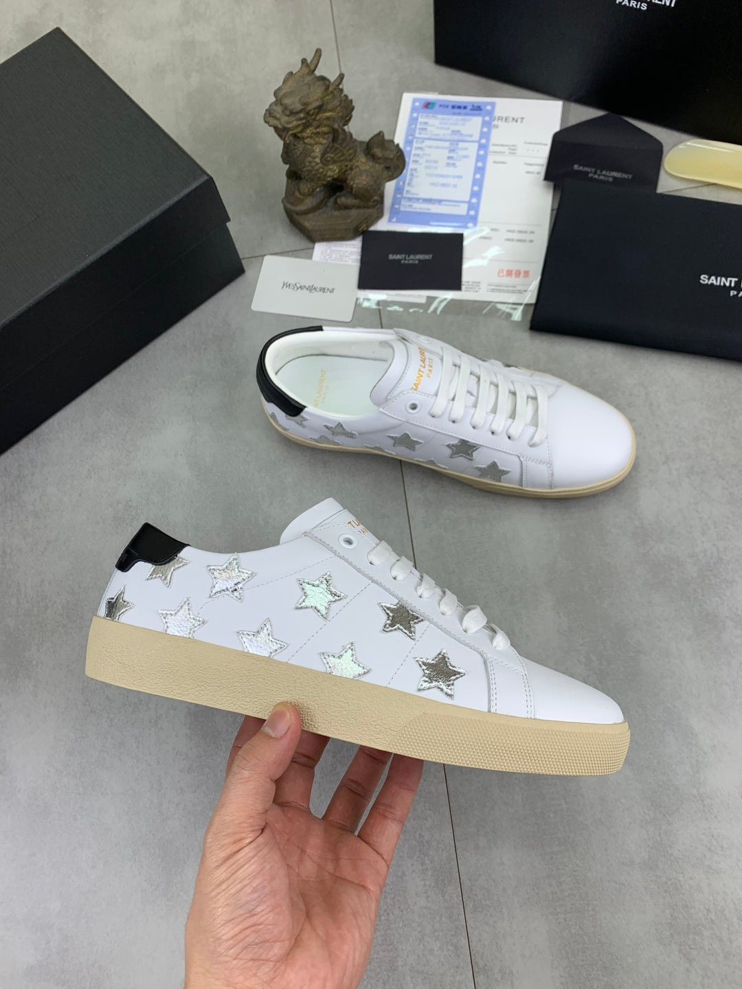 YSL unisex luxury shoes: white sneakers with star print and tan sole, hand-held view