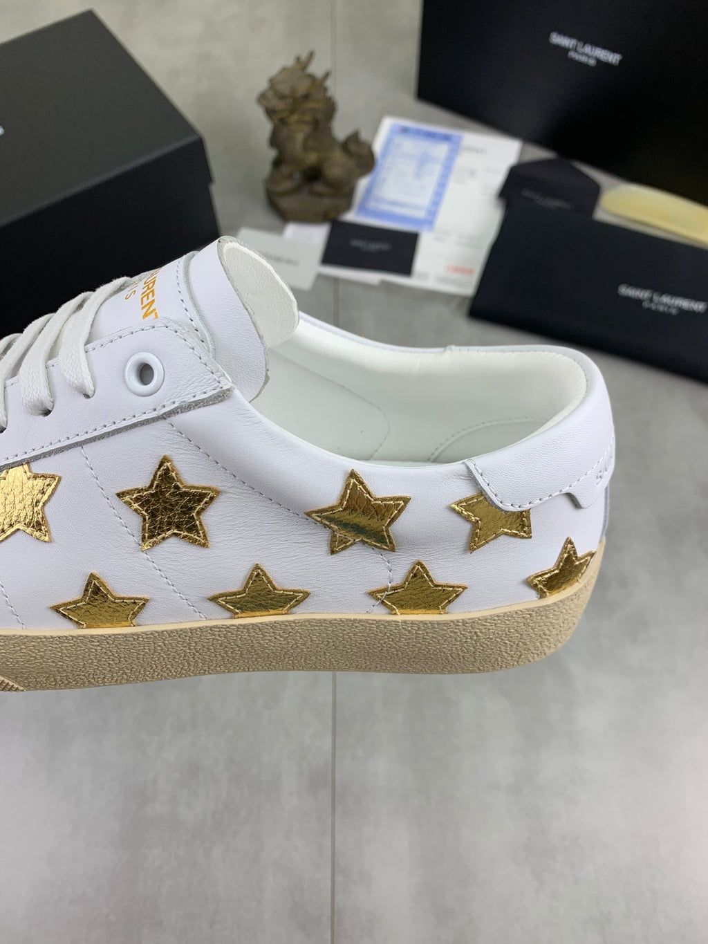 White low-top sneakers with gold stars on side, padded collar, and beige sole
