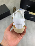 White low-top sneakers with gold trim at heel and beige rubber sole