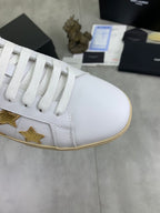 White leather sneaker with gold star trim, white laces, and beige sole edge