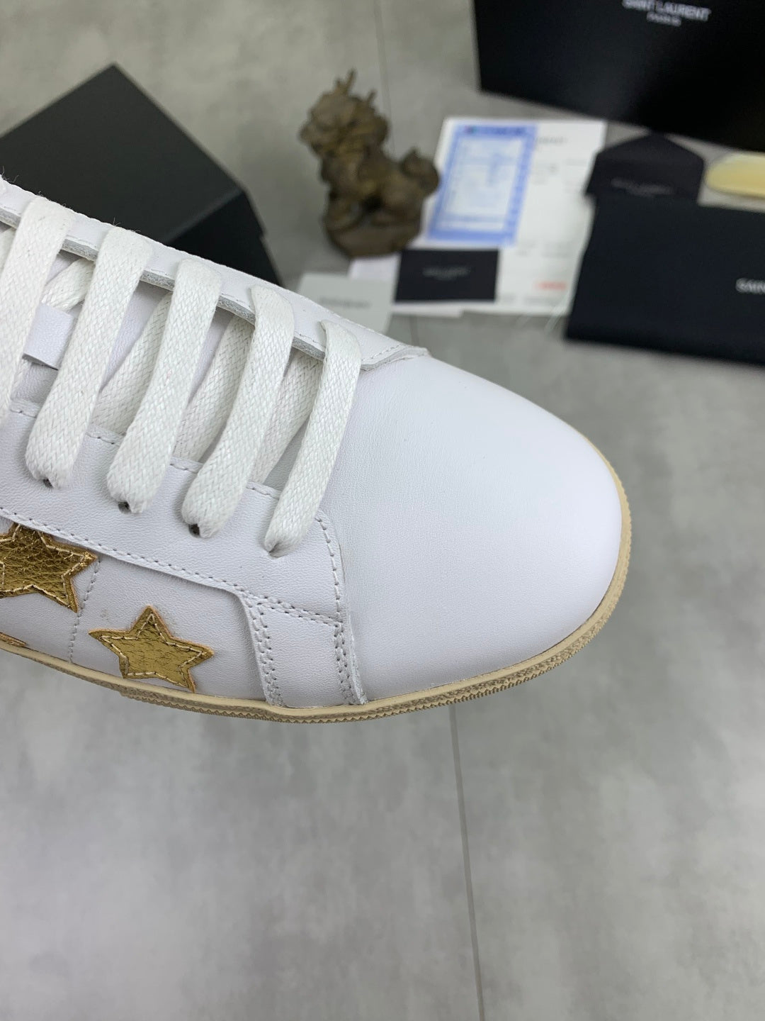 White leather sneaker with gold star trim, white laces, and beige sole edge