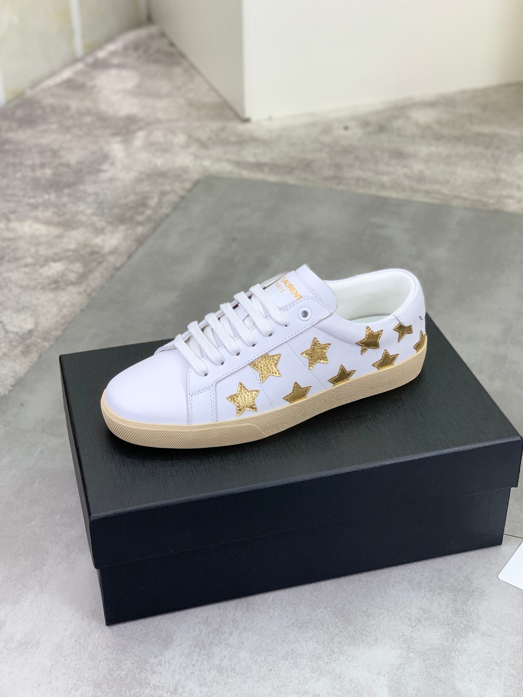 White low-top sneakers with gold star detailing and beige rubber sole