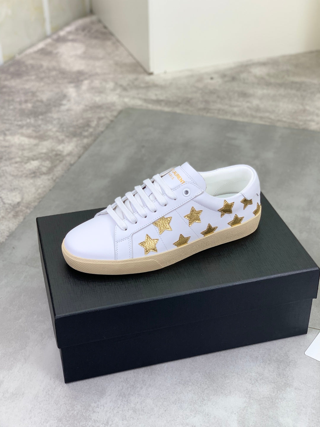 White low-top sneakers with gold star detailing and beige rubber sole