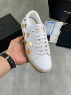 White low-top sneakers with gold star patches and beige rubber sole