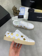 White low-top sneakers with gold star pattern and beige rubber sole, side view
