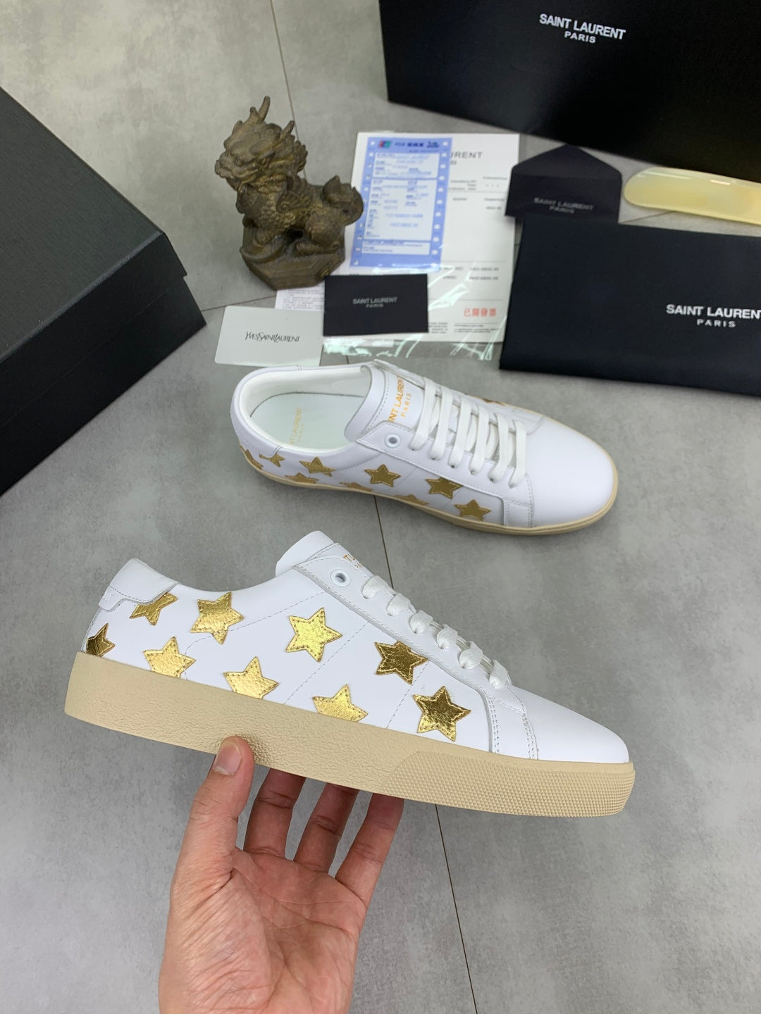 White low-top sneakers with gold star pattern and beige rubber sole, side view