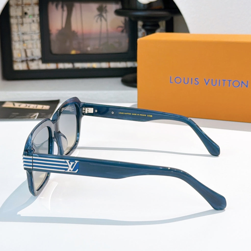 Designer sunglasses, blue frames shown from the side with gold striped temples and emblem detail.