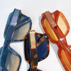 Designer sunglasses, close-up of glossy blue and amber square frames with gold striped temple emblems.