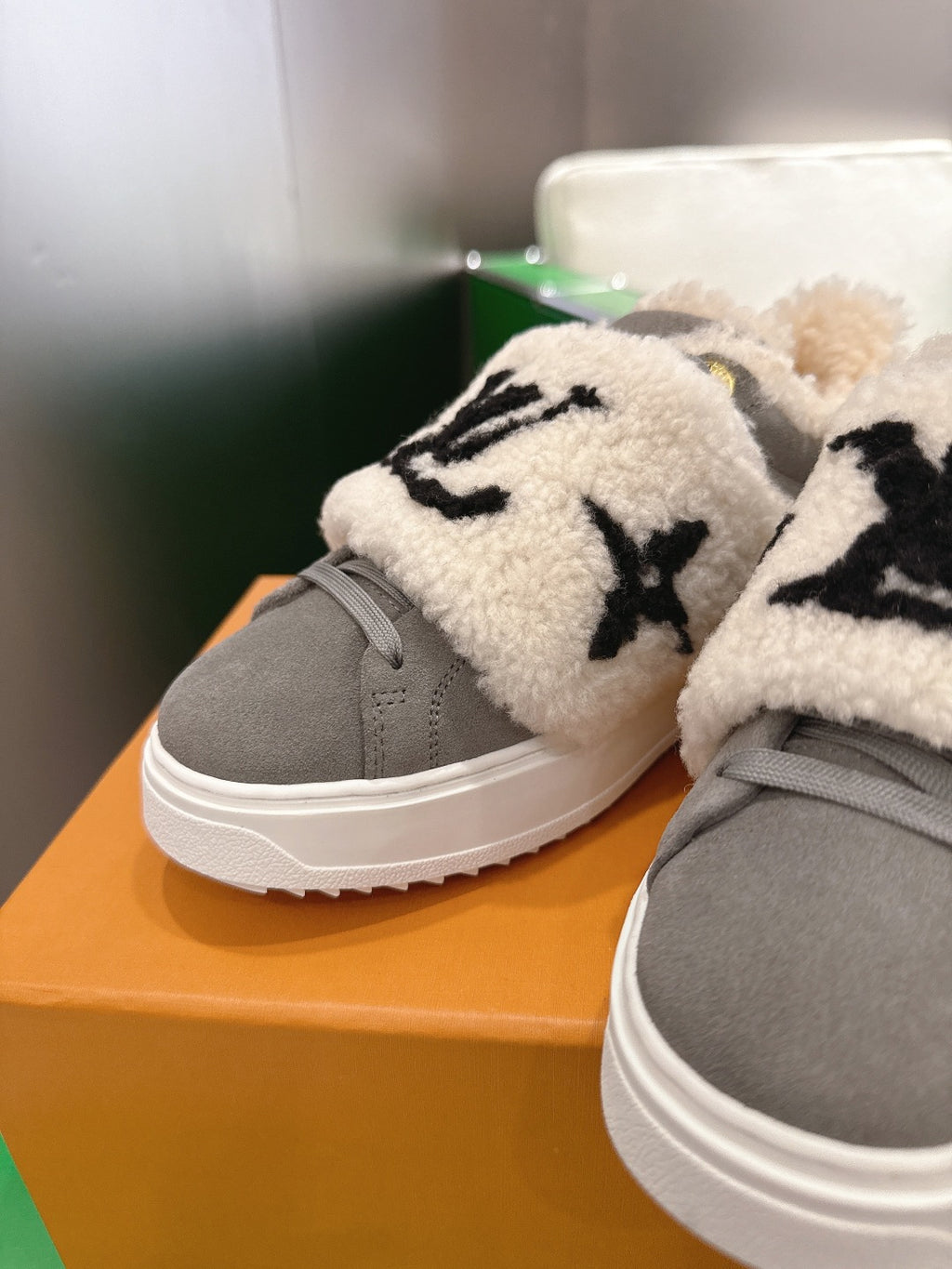 Close-up of gray sneakers with cream sherpa collar and black logo embroidery