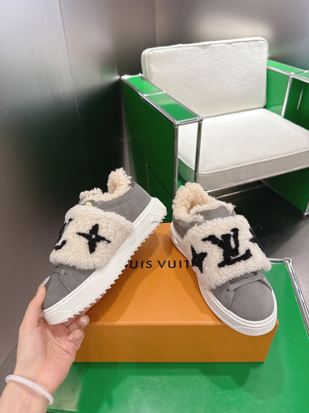 Gray low-top sneaker held in hand with cream sherpa cuff and black logo on strap