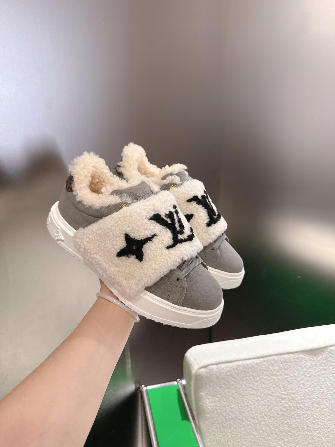 Side view of gray sneakers with cream sherpa strap and black logo patch