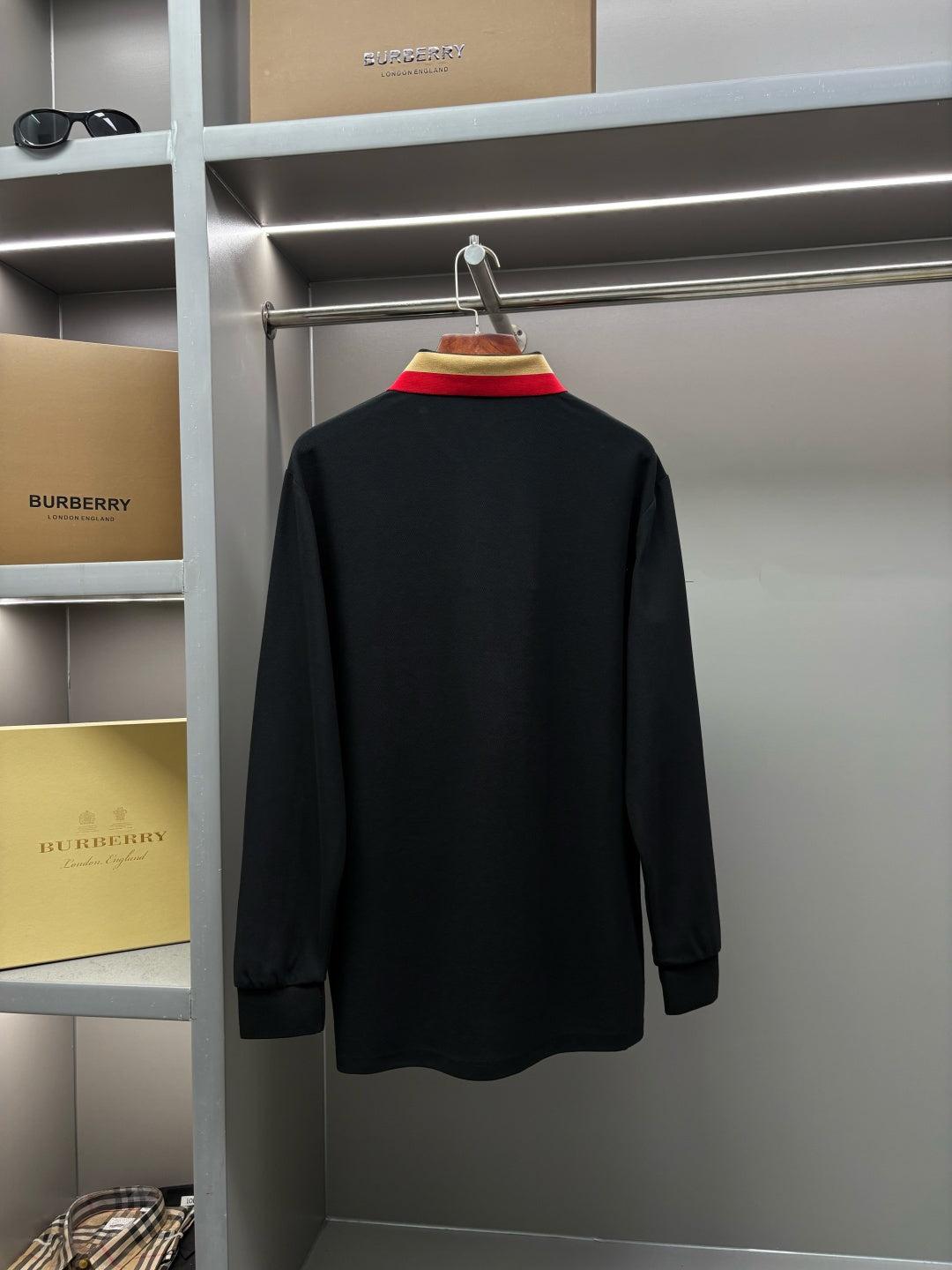 Black long-sleeve polo shirt, back view hanging on a rack