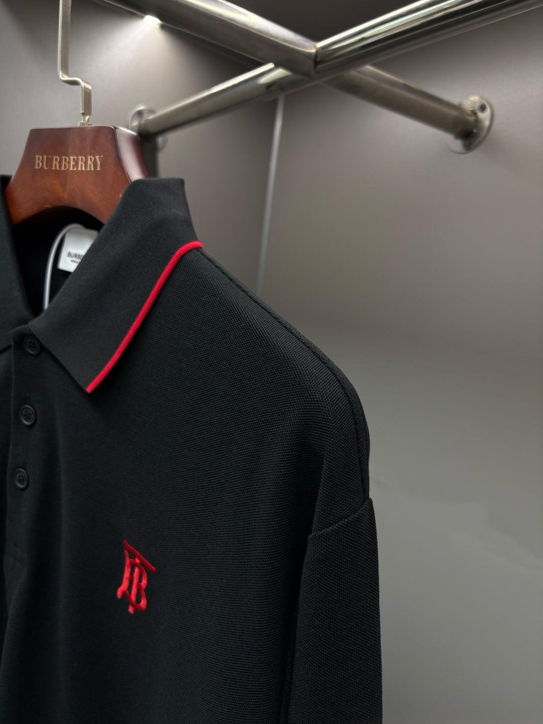 Long-sleeve polo shirt side view with small monogram logo on dark black fabric