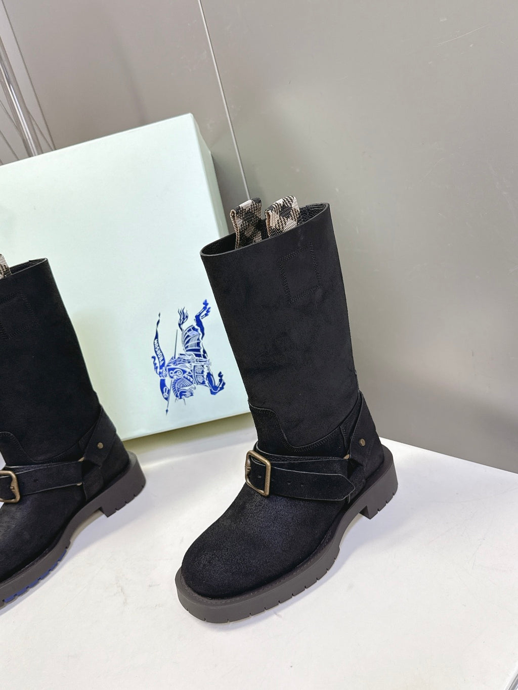Black suede mid-calf boots with tan buckle strap and patterned lining at top