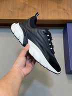 Black and dark gray Dior sneakers with white sole, held by hand, lace-up style