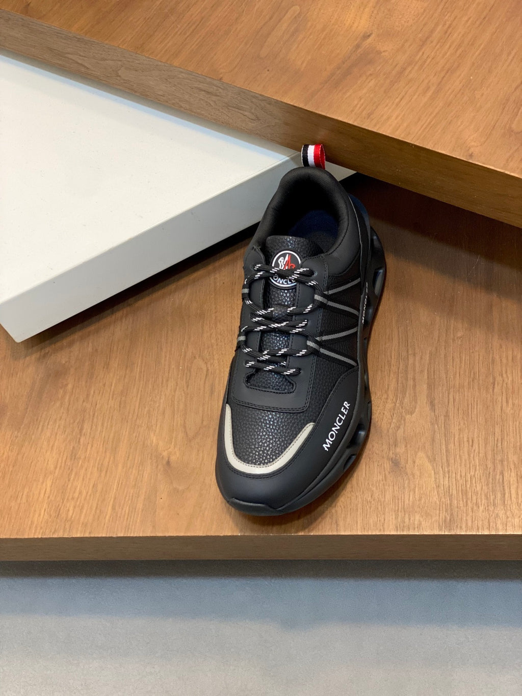 Moncler black sneaker on shelf with lace-up front and red-white heel tab
