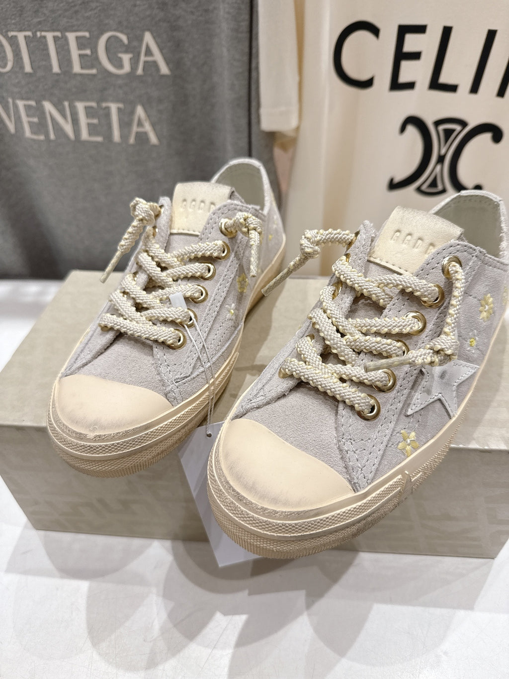 Grey low-top sneakers, side view, white laces with gold accents, beige sole