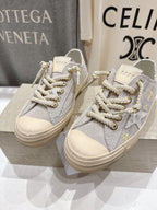 Grey low-top sneakers, side view, white laces with gold accents, beige sole