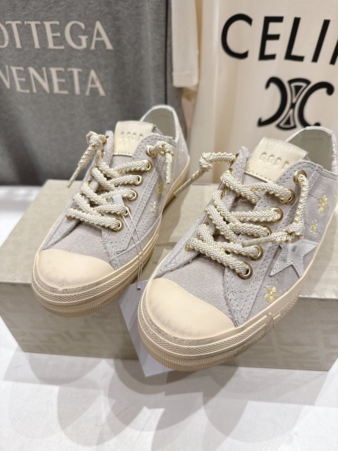 Grey low-top sneakers, side view, white laces with gold accents, beige sole
