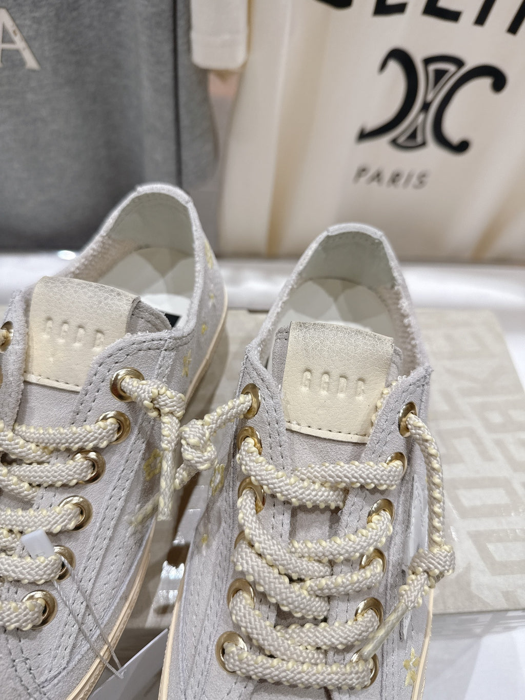 Close-up: grey low-top sneakers with white laces and gold hardware eyelets