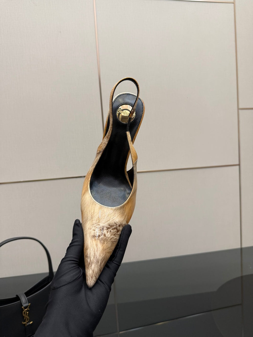 Women’s pointed-toe slingback heel held in black gloves, black and tan speckled finish