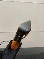 Orange patent high-heel shoe sole and heel bottom, held in black-gloved hand