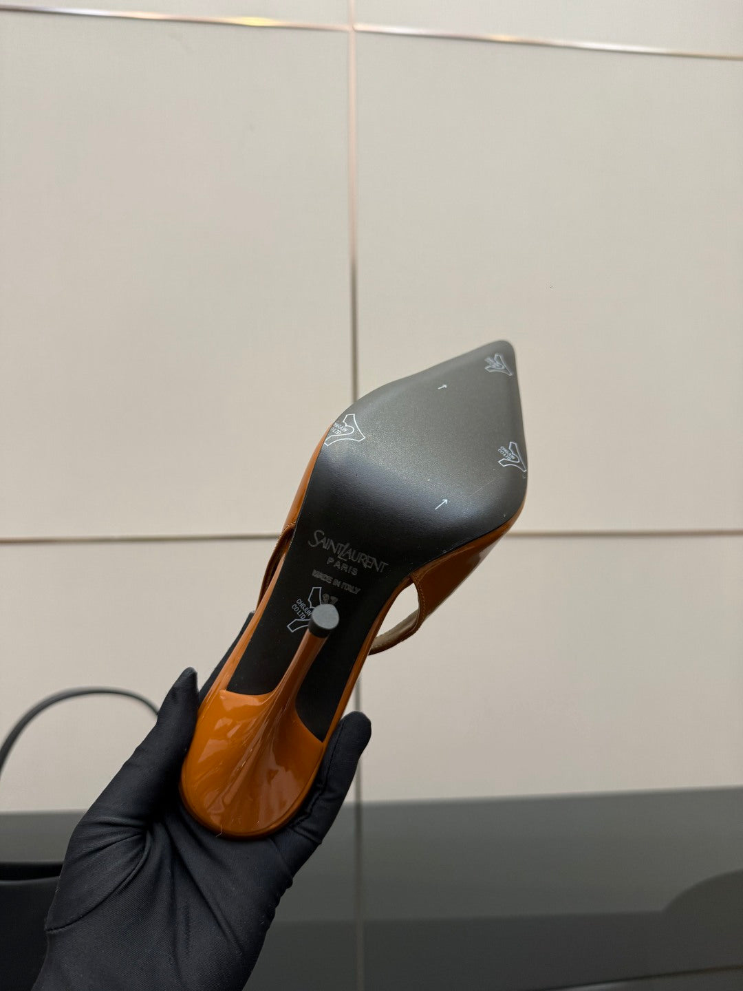 Orange patent high-heel shoe sole and heel bottom, held in black-gloved hand