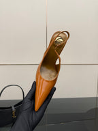 Tan-orange patent pointed-toe slingback high heel, held in black-gloved hand