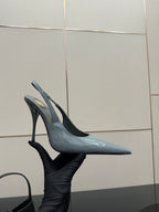 Light blue glossy pointed-toe slingback stiletto heels held in hand, high heel.