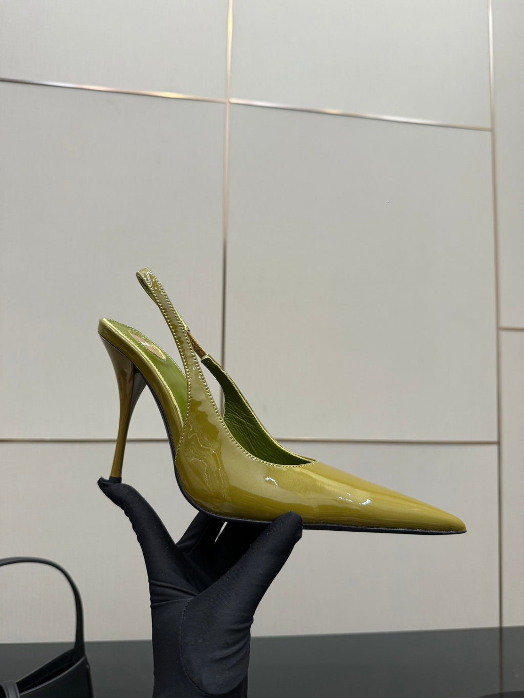 Lime-green patent pointed-toe stiletto heel, side view held by a glove