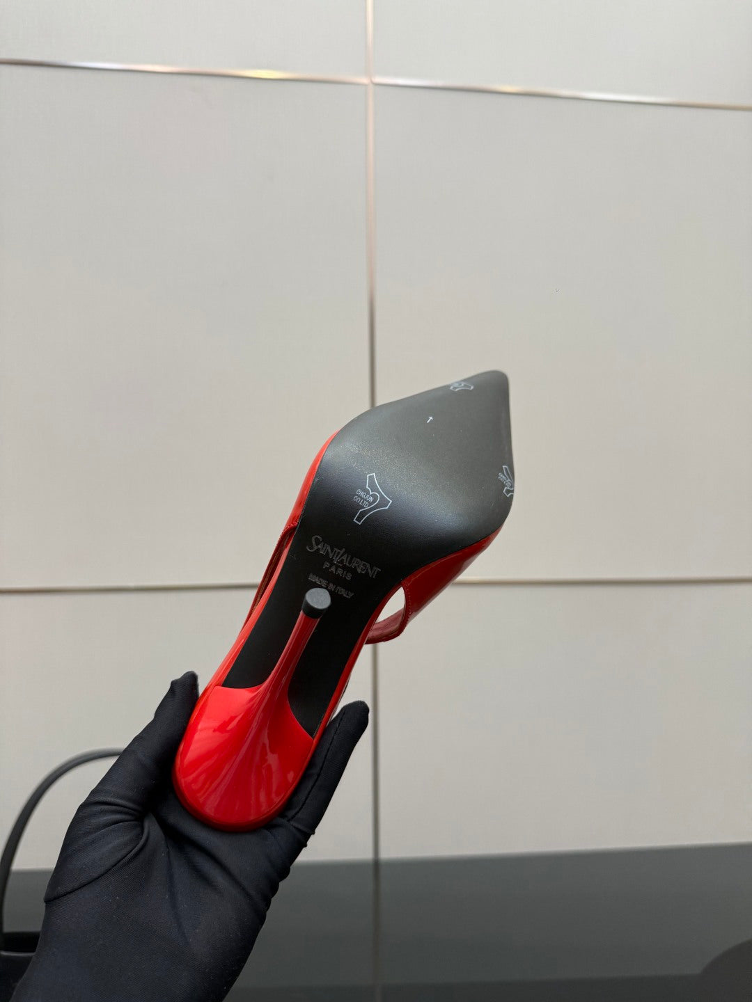 Red patent pointed-toe stiletto pump close-up held in a black-gloved hand