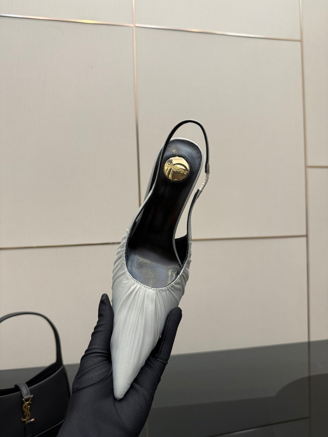 YSL ladies white slingback heel on black-gloved hand, showing gold emblem on toe