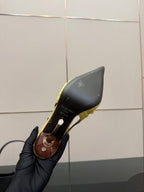 Yellow slingback stiletto heel shoe sole and heel underside in close-up, held by gloved hand