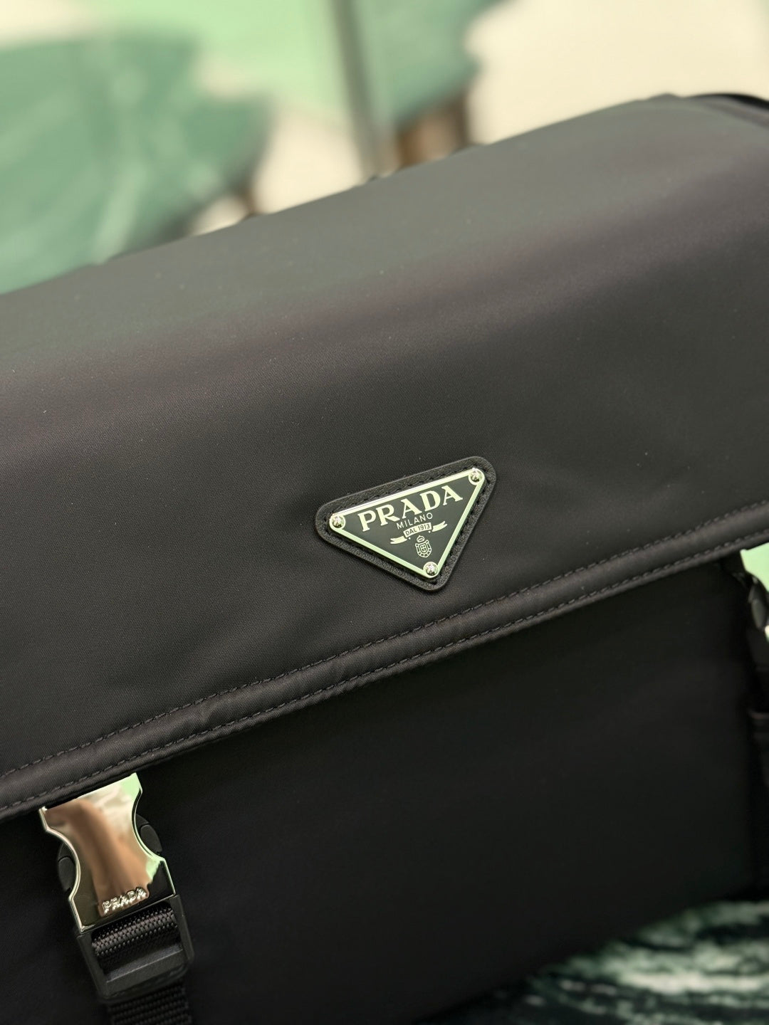 Black Prada bag close-up of front flap logo plate on smooth fabric.