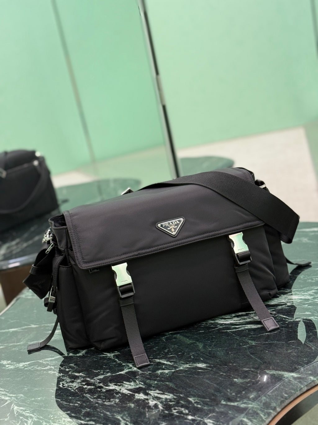 Black Prada messenger bag side view with front flap and adjustable shoulder strap.