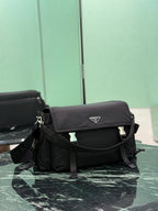 Black Prada messenger bag angled view, front flap with logo plate and buckled straps.