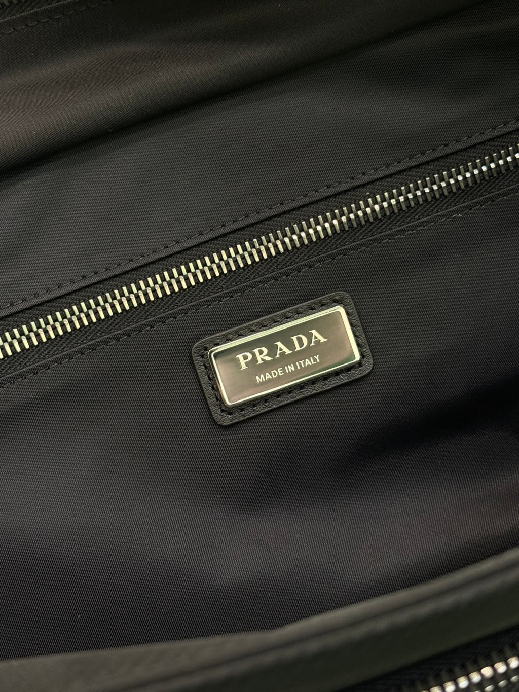 Black Prada bag close-up of gold zipper track and logo plate on flap.