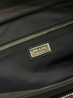 Black Prada bag close-up of gold zipper track and logo plate on flap.