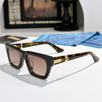 Black square sunglasses with gold-tone accents and tinted lenses; tortoiseshell temples