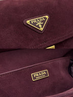 Burgundy suede Prada bag close-up with triangle logo plaque and gold trim buckles