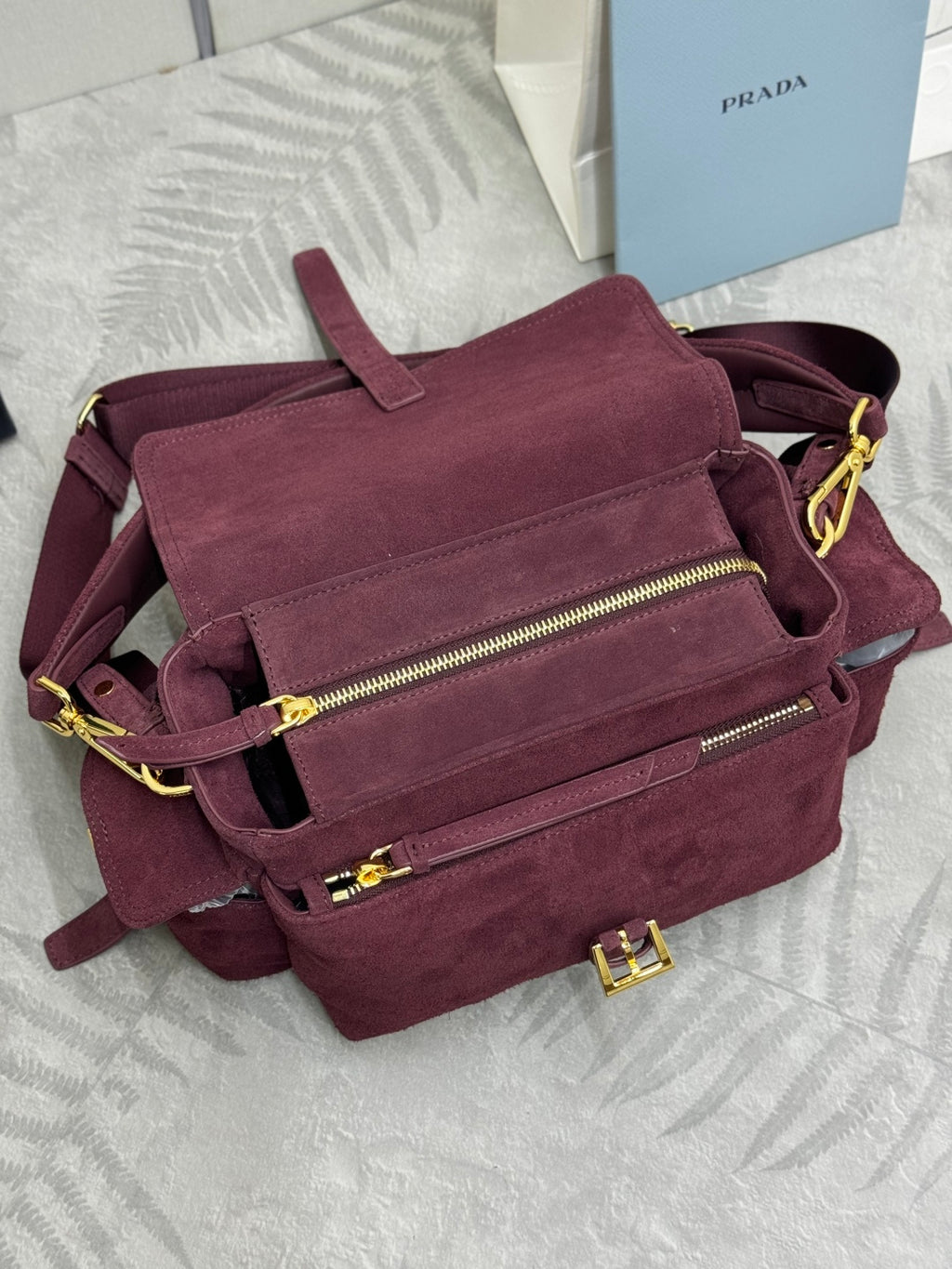 Burgundy suede Prada crossbody bag with two zip pockets and gold hardware details