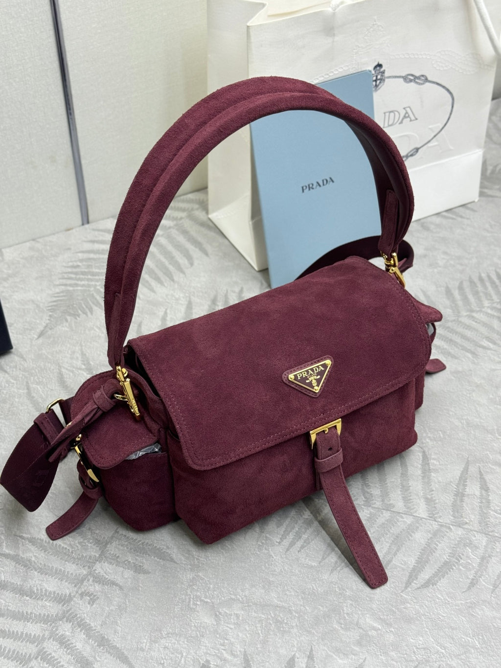 Burgundy suede Prada crossbody bag with front flap, gold clasp, and adjustable strap