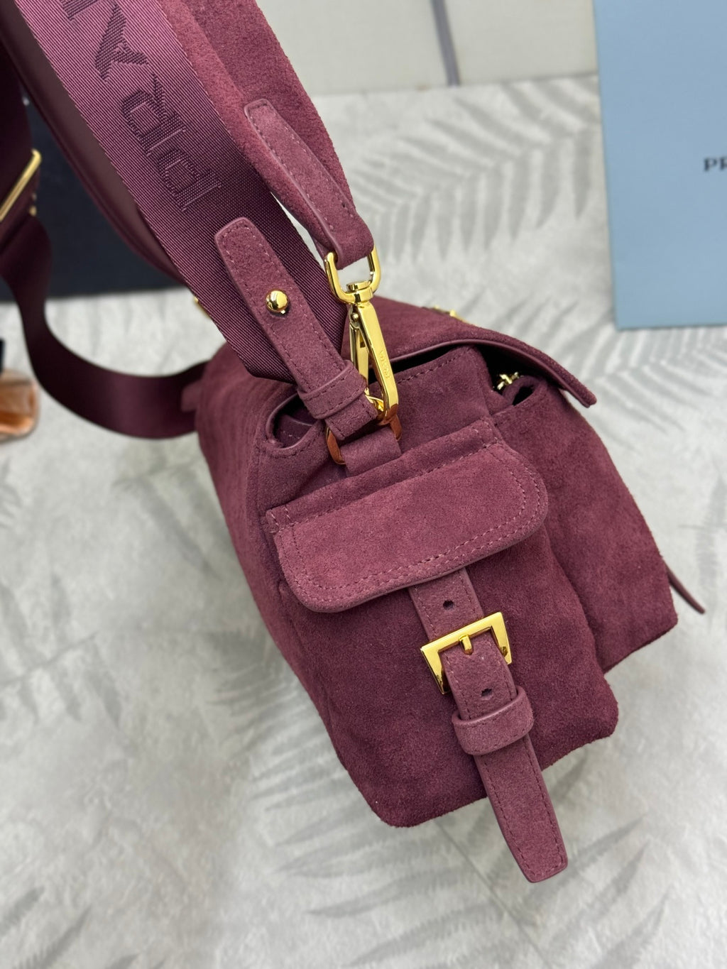 Burgundy suede Prada mini bag with front pocket, gold chain accents, and zip closure
