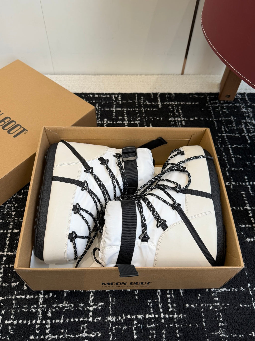 White and black lace-up winter boots in a box, showing rounded toe and padded collar