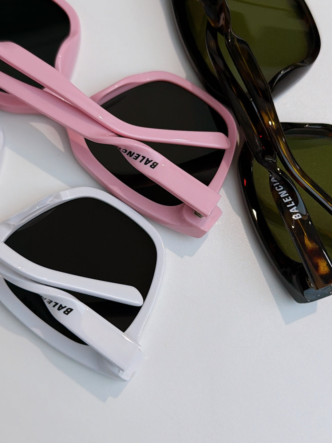 Balenciaga sunglasses close-up: pink strap and white frames with dark lenses.