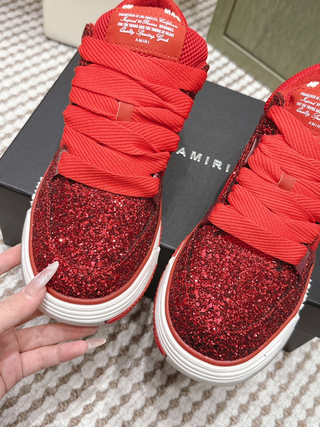 Front view of red glitter lace-up sneakers with white sole and Amiri logo, held